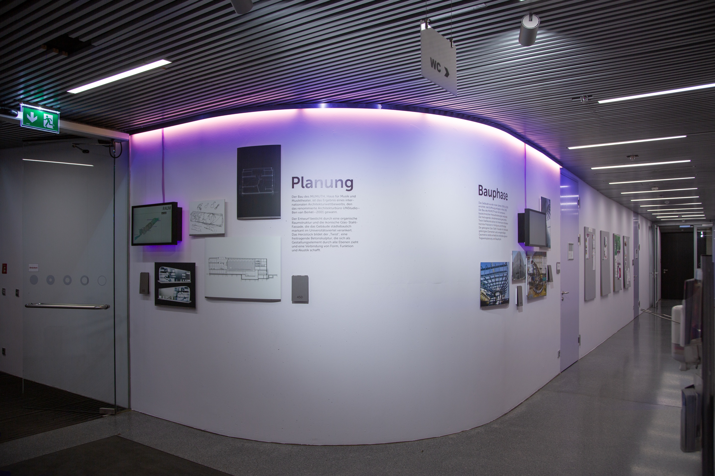 The exhibition wall in the MUMUTH entrance hall, lit in purple, with the sections Planung and Bauphase.