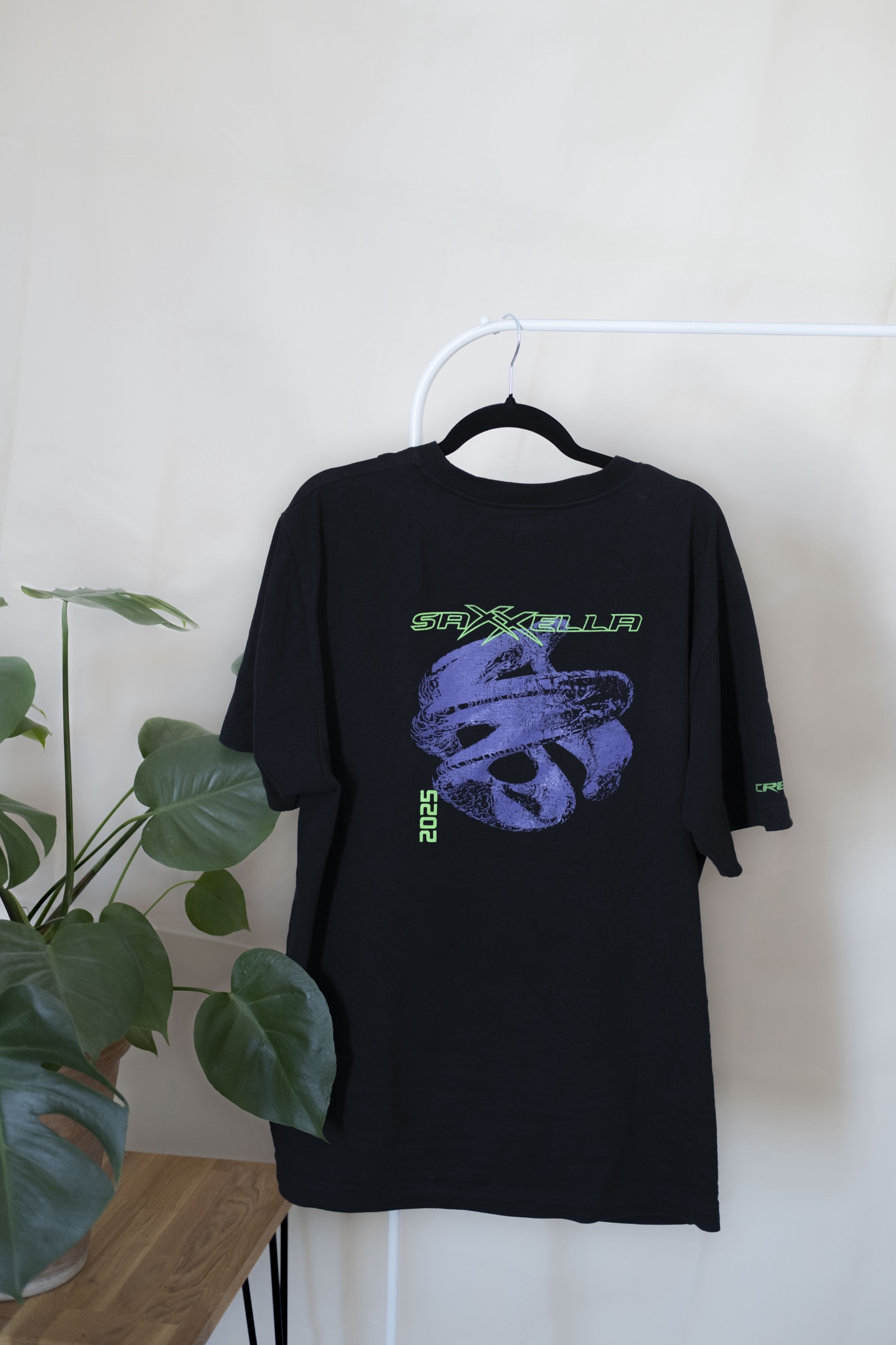 Black saXXella T-shirt with the festival graphic on a hanger